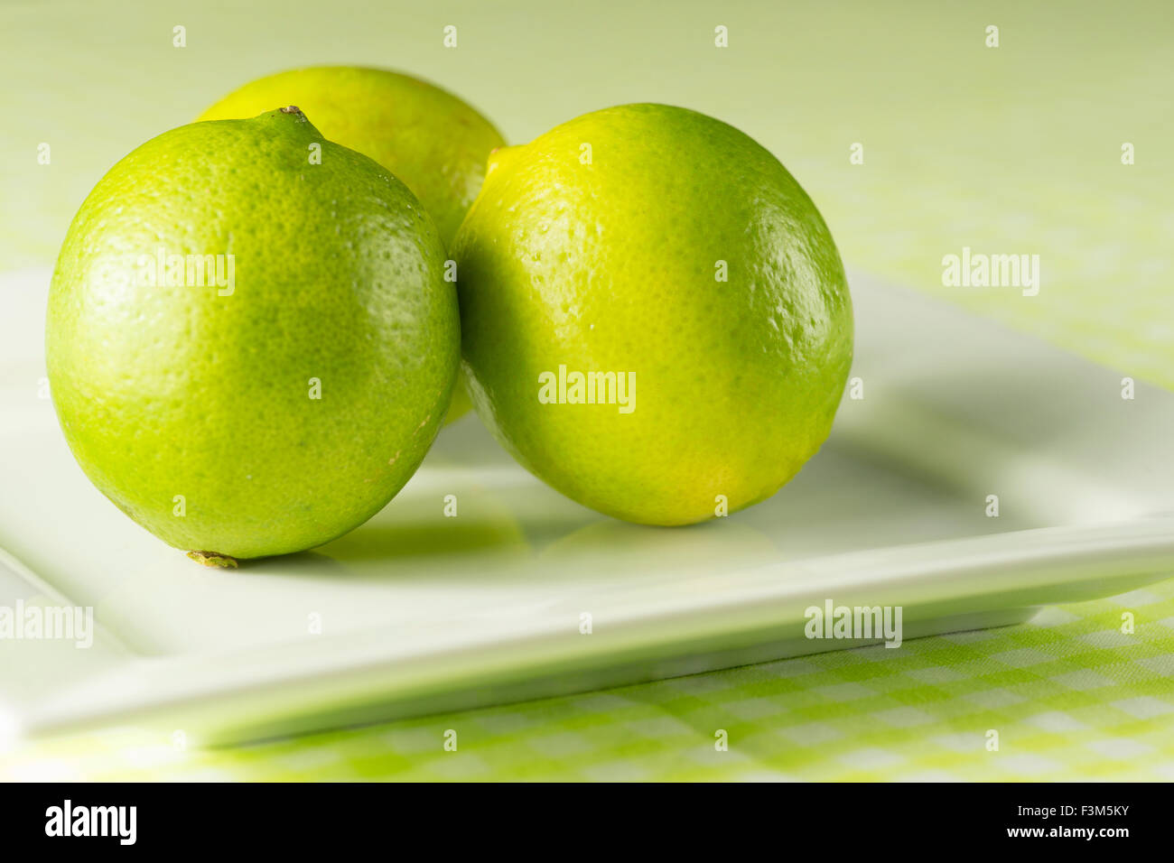 Frischen grünen Limetten auf einem weißen Teller gegen einen sommerlich grünen Hintergrund und karierten Tischdecke Stockfoto