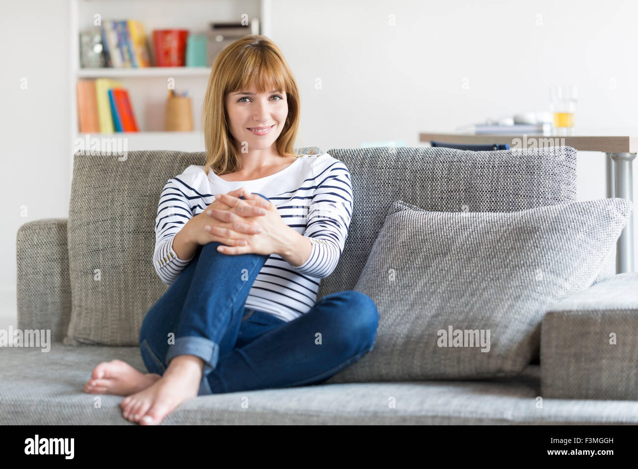 Natürliche 30-Jahr-alte Frau sitzt auf der Couch im modernen Haushalt. Aussehende Kamera Stockfoto