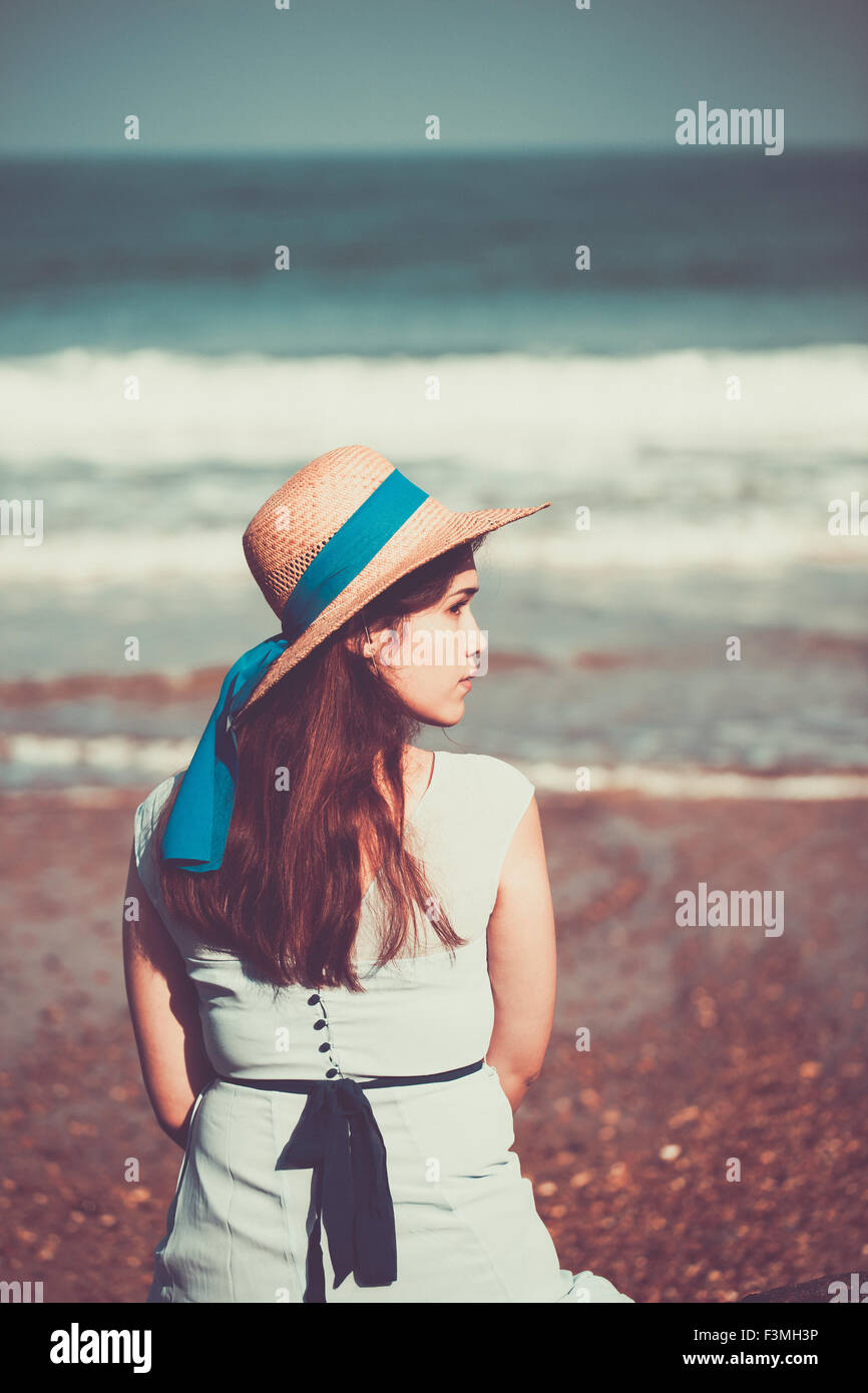 Schöne historische Mädchen sitzen am Strand in einem blauen Kleid und trägt einen Strohhut Stockfoto