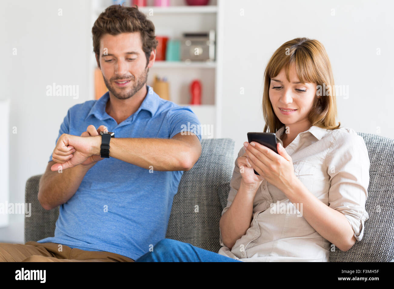 Digitale Geek zu zweit am Hone auf Couch mit Smartwatch En Handy Stockfoto