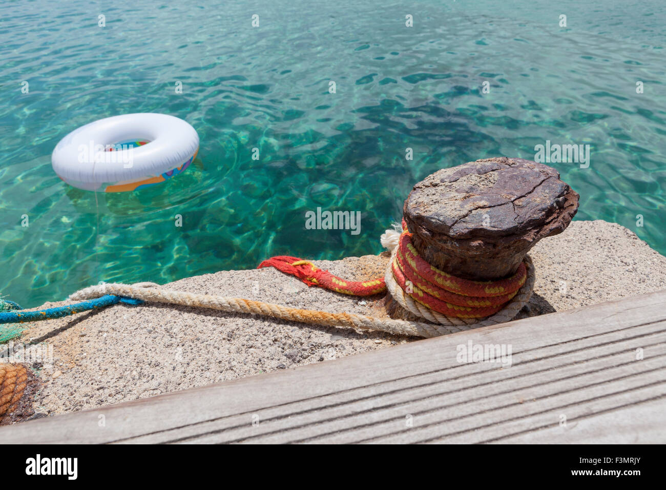 Nahaufnahme von einem rostigen Poller und Seile mit ein Lebensretter im Wasser im Hintergrund Stockfoto