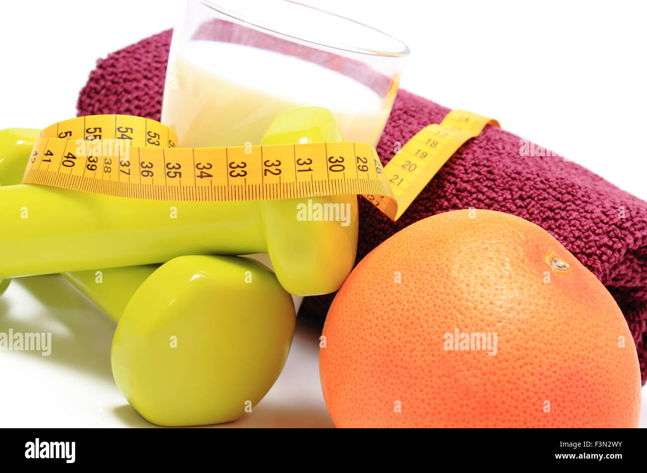 Grüne Hanteln und lila Handtuch für den Einsatz in Fitness, frische Grapefruit, Glas Milch und Maßband, Konzept zum Abnehmen Stockfoto