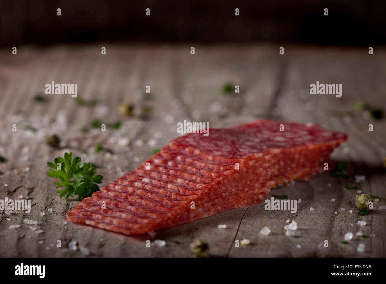 In Scheiben geschnitten quadratische Salami auf Holz Hintergrund mit Gewürzen Stockfoto