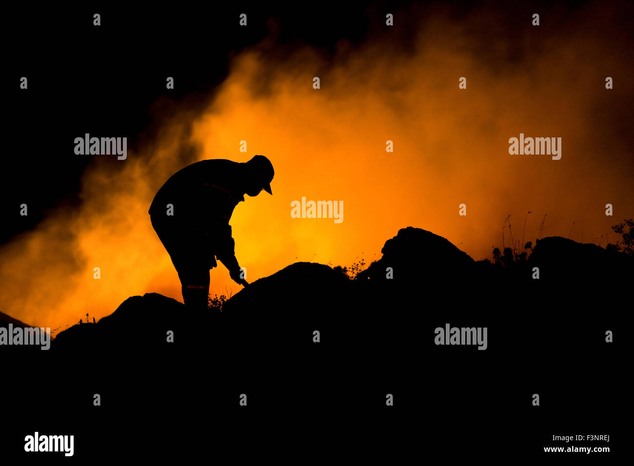 Hintergrundbeleuchtung durch brennende Flamme Rauch, Shilhouette Feuerwehrmann, trägt einen kleinen Rauchschutz-Maske im Gesicht beim Löschangriff. Stockfoto