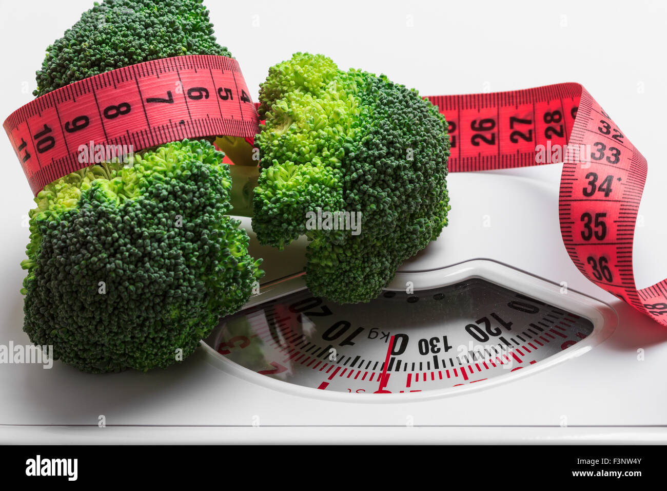 Eine Diät, gesunde Ernährung Gewicht Steuerungskonzept abspecken. Closeup grünen Brokkoli mit Maßband auf weißen Schuppen Stockfoto