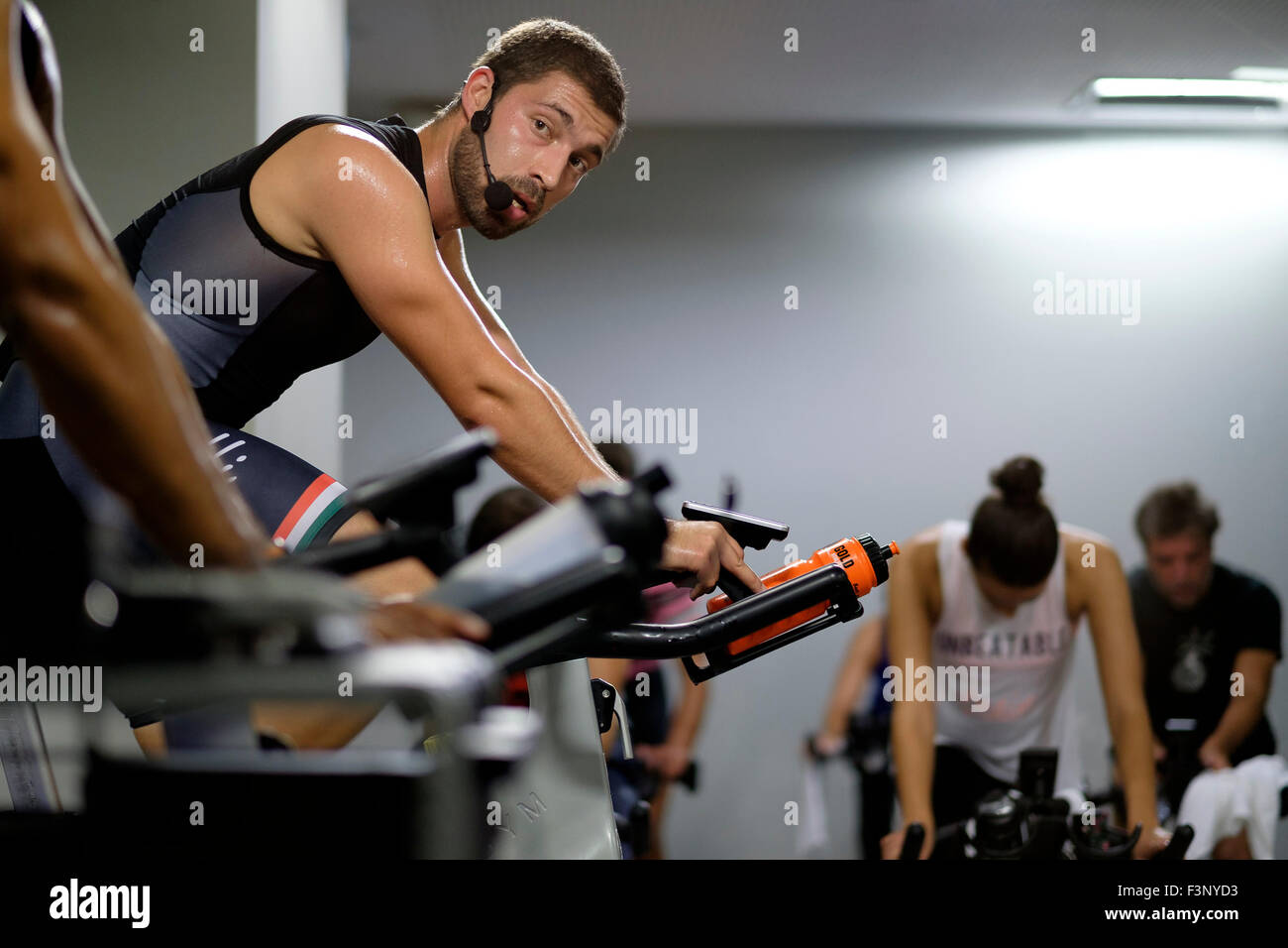Fitness-Trainer vor Menschen auf stationären Fahrrädern während einem Spinning Kurs in der Turnhalle Stockfoto