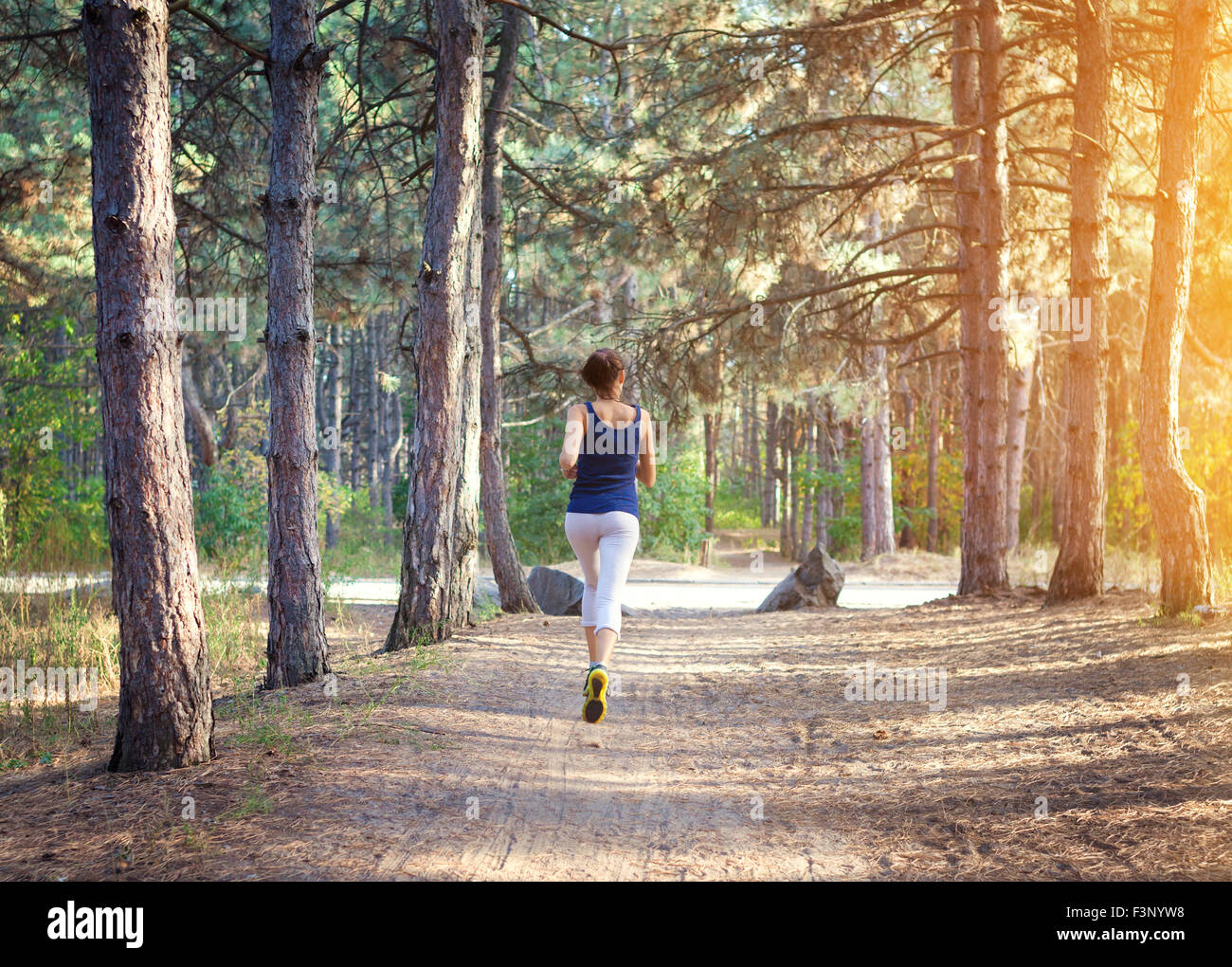 Junge Frau auf einer Landstraße bei Sonnenuntergang im herbstlichen Wald ausgeführt. Lifestyle-Sport-Hintergrund Stockfoto