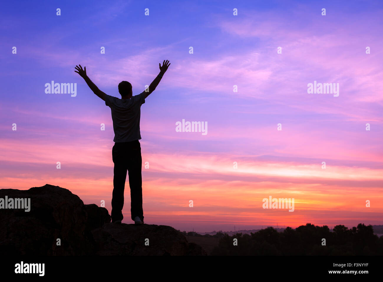 Silhouette eines Mannes mit angehoben bis Armen an den wunderschönen Sonnenuntergang auf dem Berg. Hintergrund Stockfoto