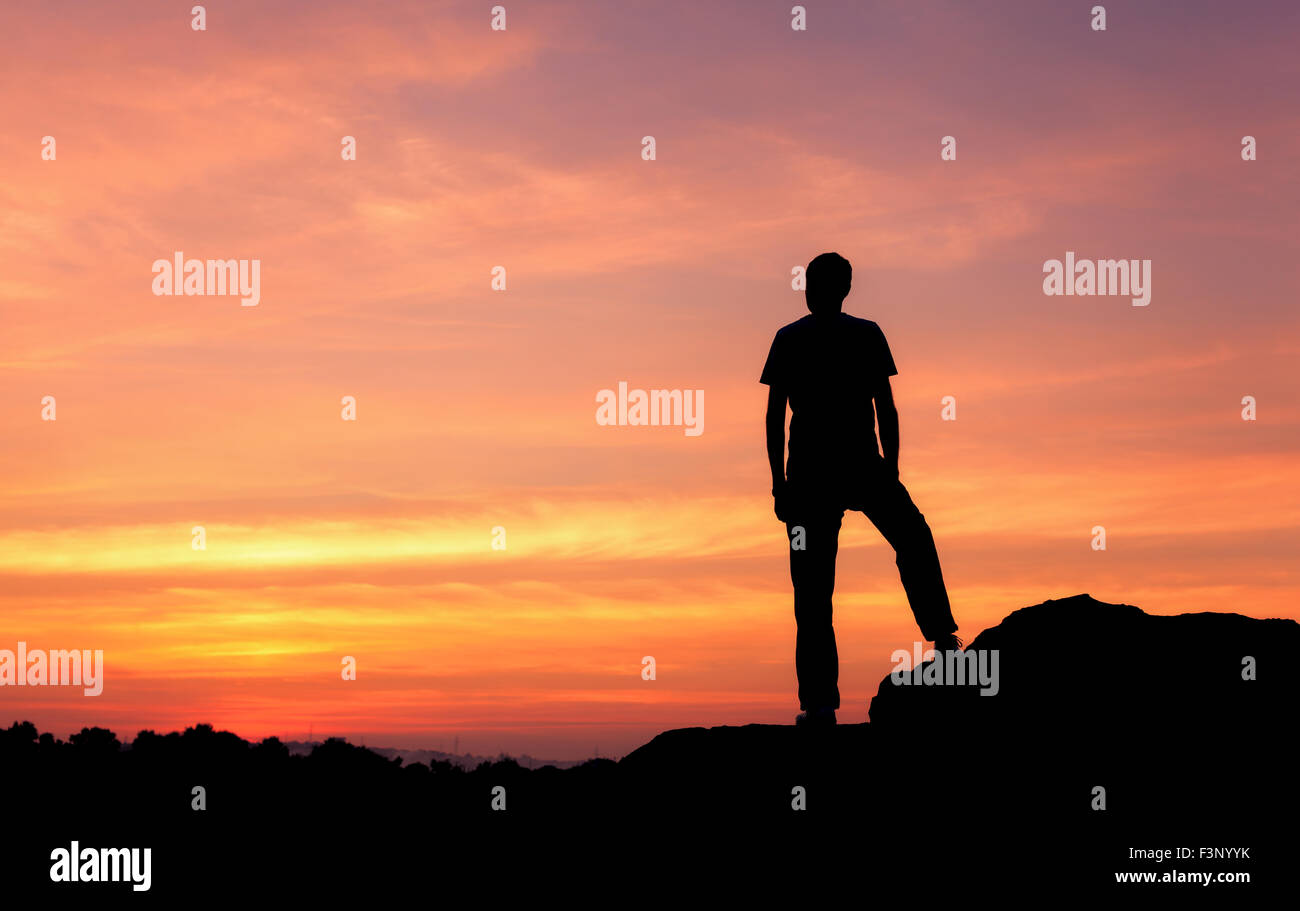 Silhouette eines Mannes mit angehoben bis Armen an den wunderschönen Sonnenuntergang auf dem Berg. Hintergrund Stockfoto