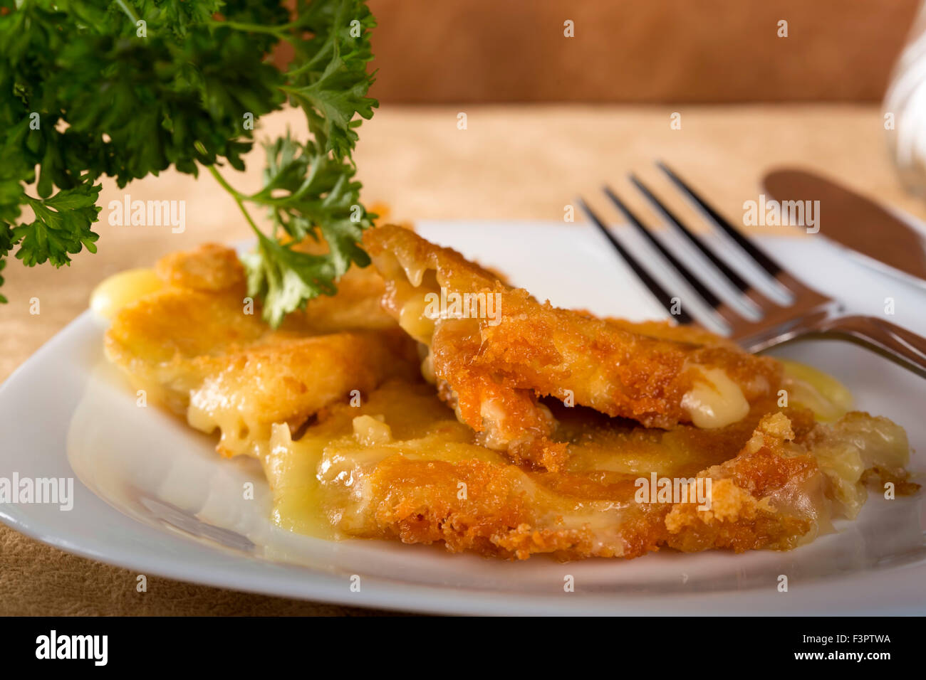 Panierter Käse auf weißen Teller mit Messer und Gabel Stockfoto