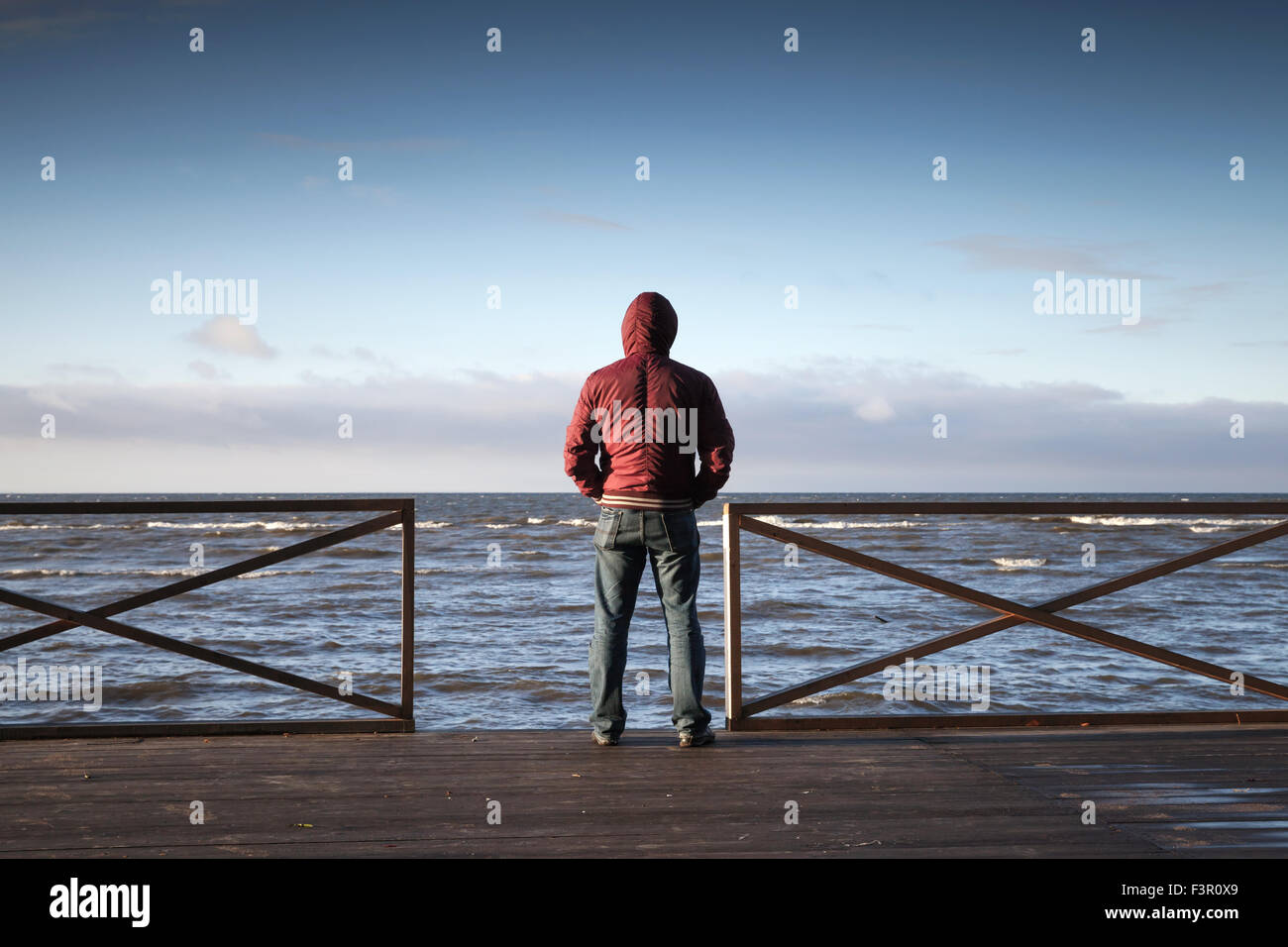 Junger Mann in Haube Blick auf das Meer von Holzsteg am Morgen. Hintere Ansicht Foto Stockfoto