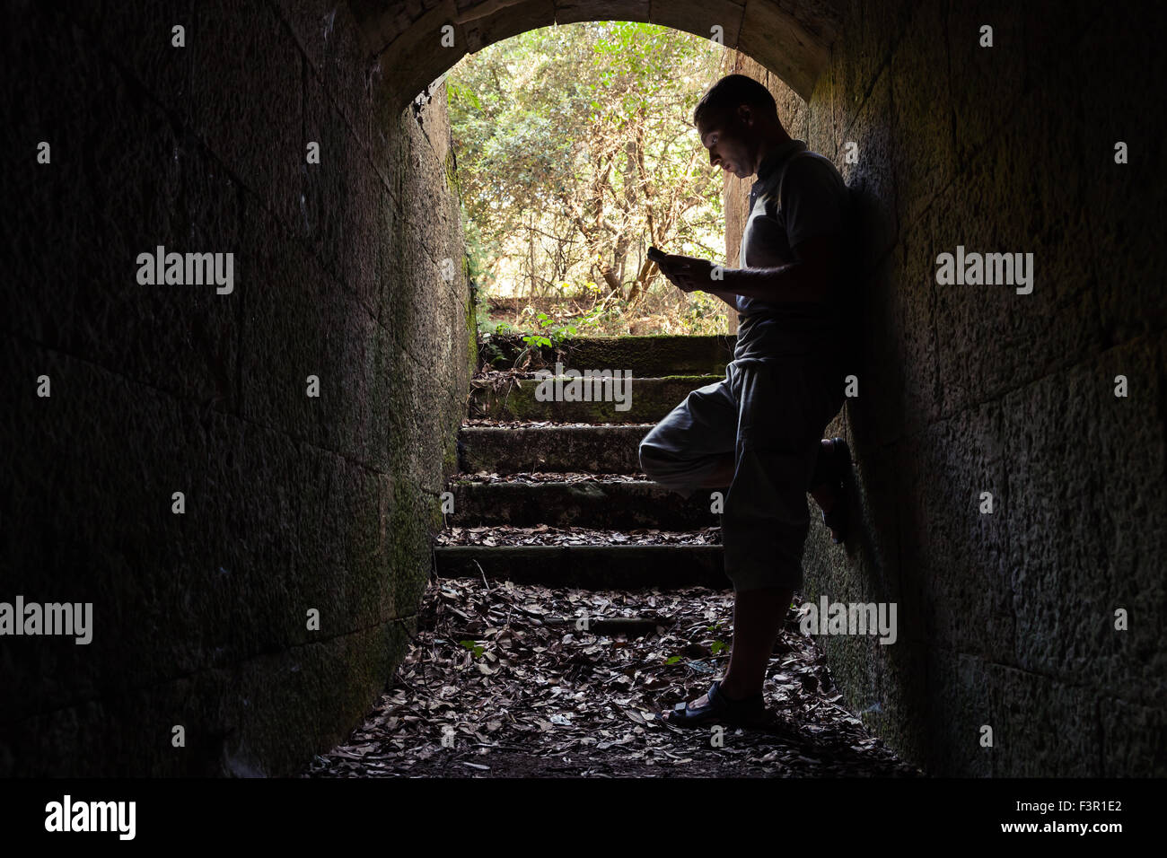 Junger Mann arbeitet auf einem Smartphone in dunklen Stein-tunnel Stockfoto