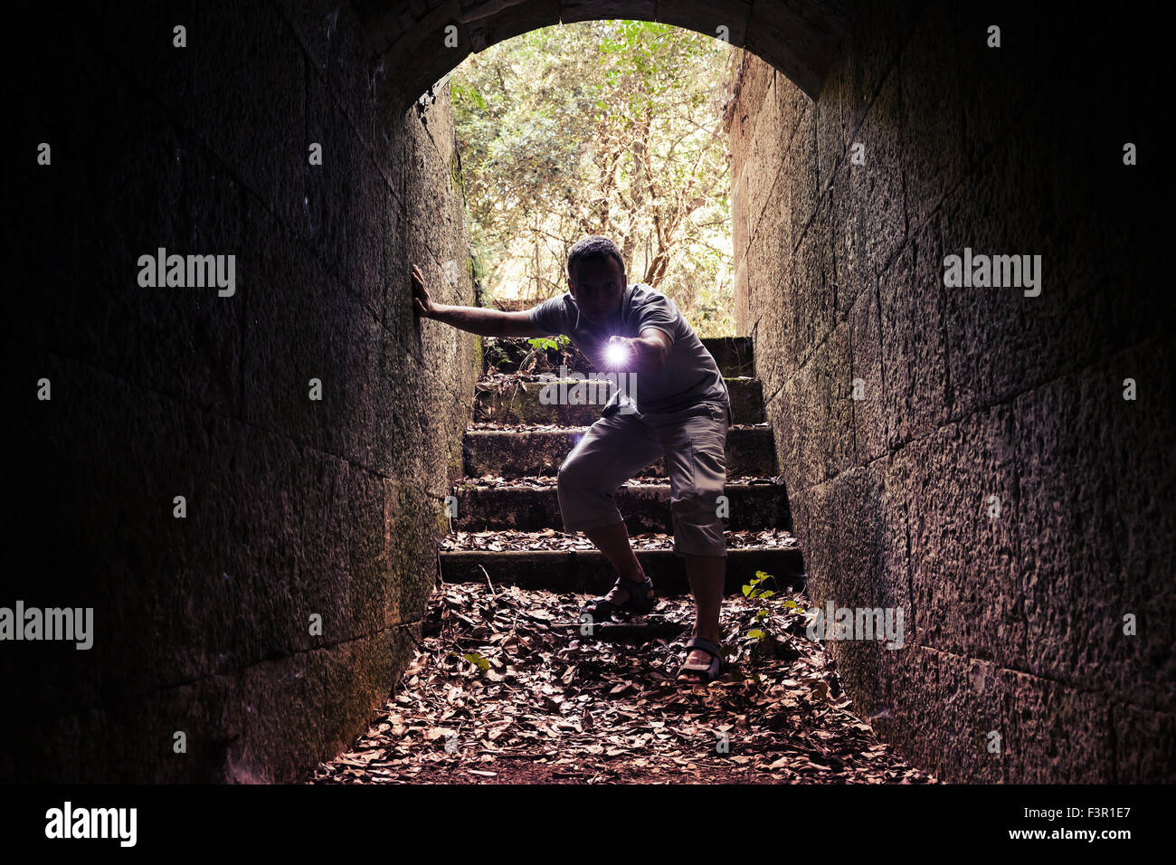 Junger Mann mit einer Taschenlampe dunklen Stein Tunnel betritt und sieht im Inneren mit Aufmerksamkeit und Angst Stockfoto