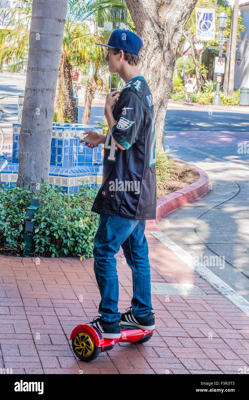 Eine Teenager prüft sein Smartphone, er balanciert auf einem elektrisch angetriebenen Scooters Board in Santa Barbara, Kalifornien. Stockfoto