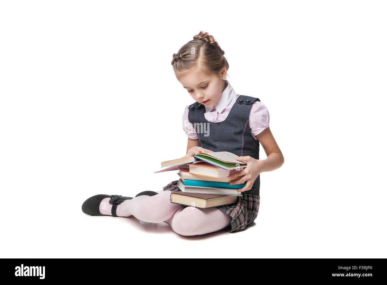 Wunderschönes kleines Mädchen in Schuluniform mit Büchern auf dem Boden sitzend Stockfoto