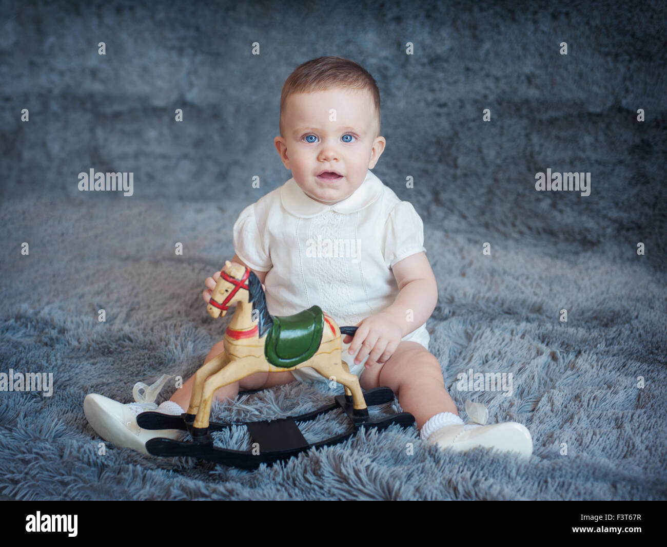Süsser Boy auf einem grauen Hintergrund mit einem Spielzeugpferd in seinen Händen Stockfoto