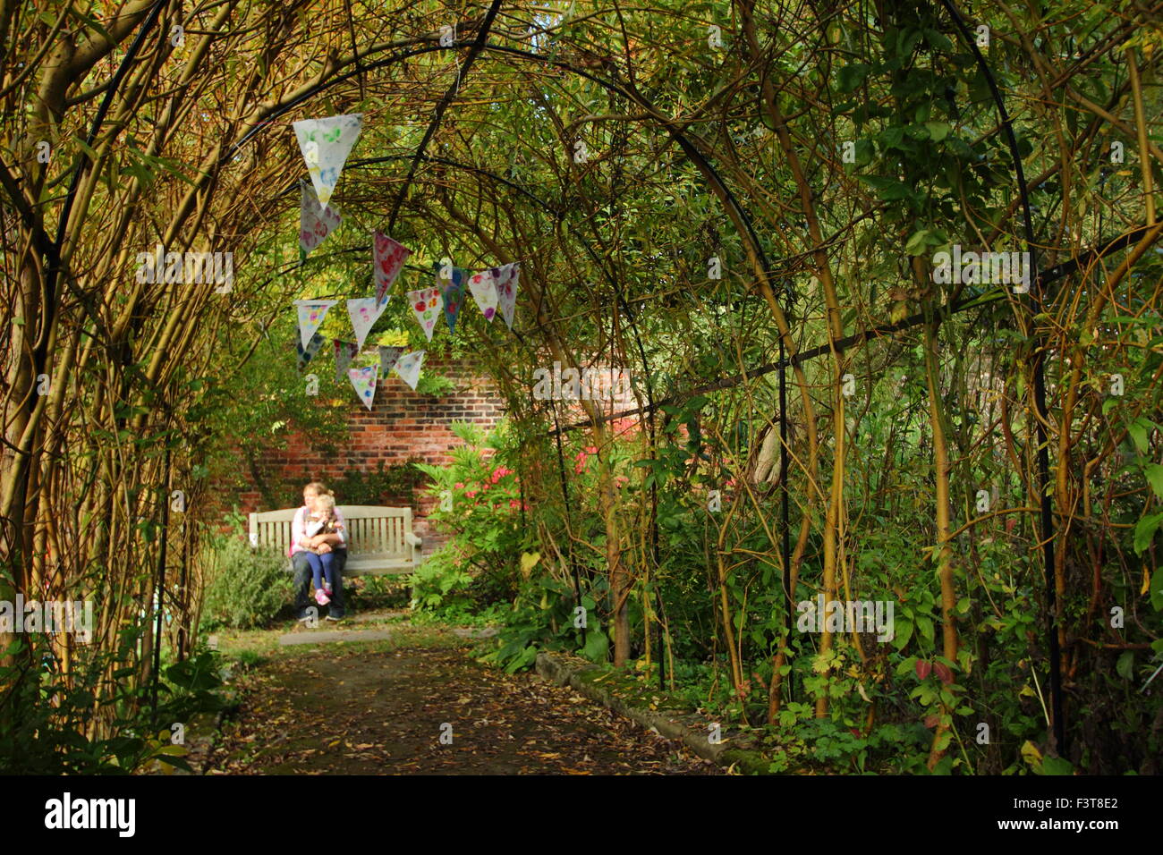 Ein Weide-Bogen geformt wie ein Tunnel eine Gartenbank in einem ummauerten Garten umrahmt, wo eine Frau und Kind Sheffield Yorkshire UK ausruhen Stockfoto