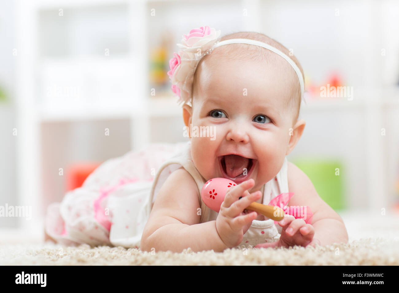 Lächelndes Mädchen schönes Kind mit Spielzeug auf Teppich liegt Stockfoto