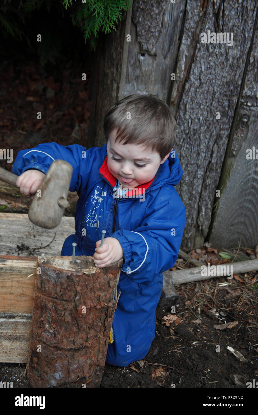 Kleiner Junge lernen, wie man Hammer verwenden, um Nagel ins Holz zu klopfen Stockfoto