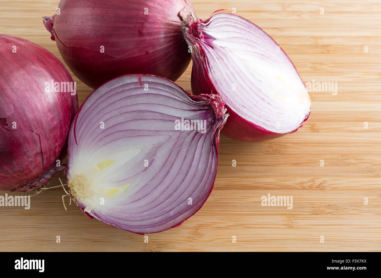 Eine große rote Zwiebel, die in zwei Hälften auf ein Holz Schneidebrett mit zwei zusätzlichen Zwiebeln an der Seite in Scheiben geschnitten Stockfoto