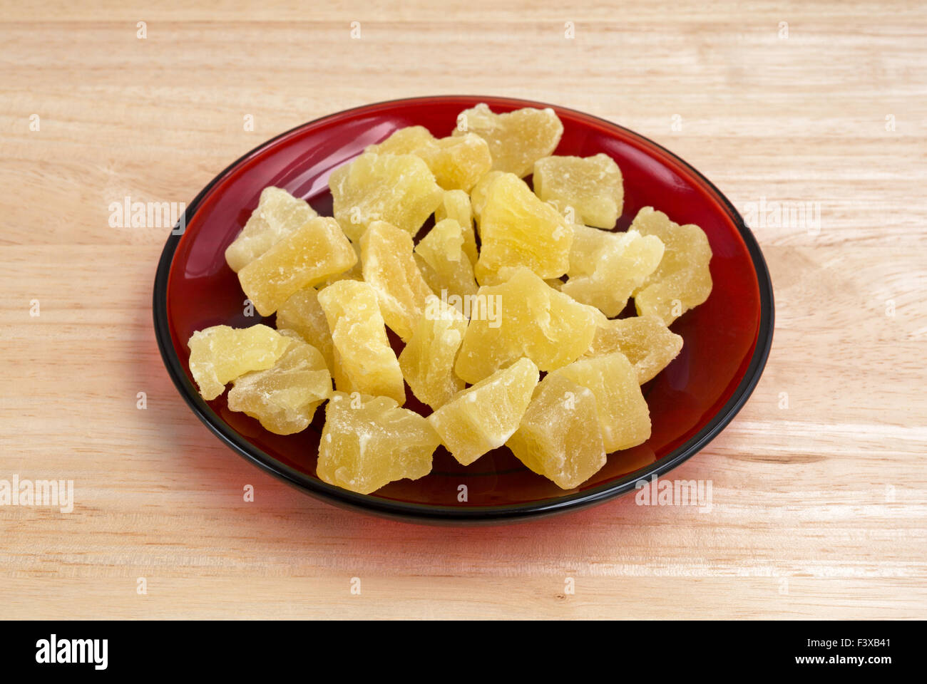 Eine Portion getrocknete gezuckerte Ananas Stücke auf einer roten Schale auf einer hölzernen Tischplatte. Stockfoto