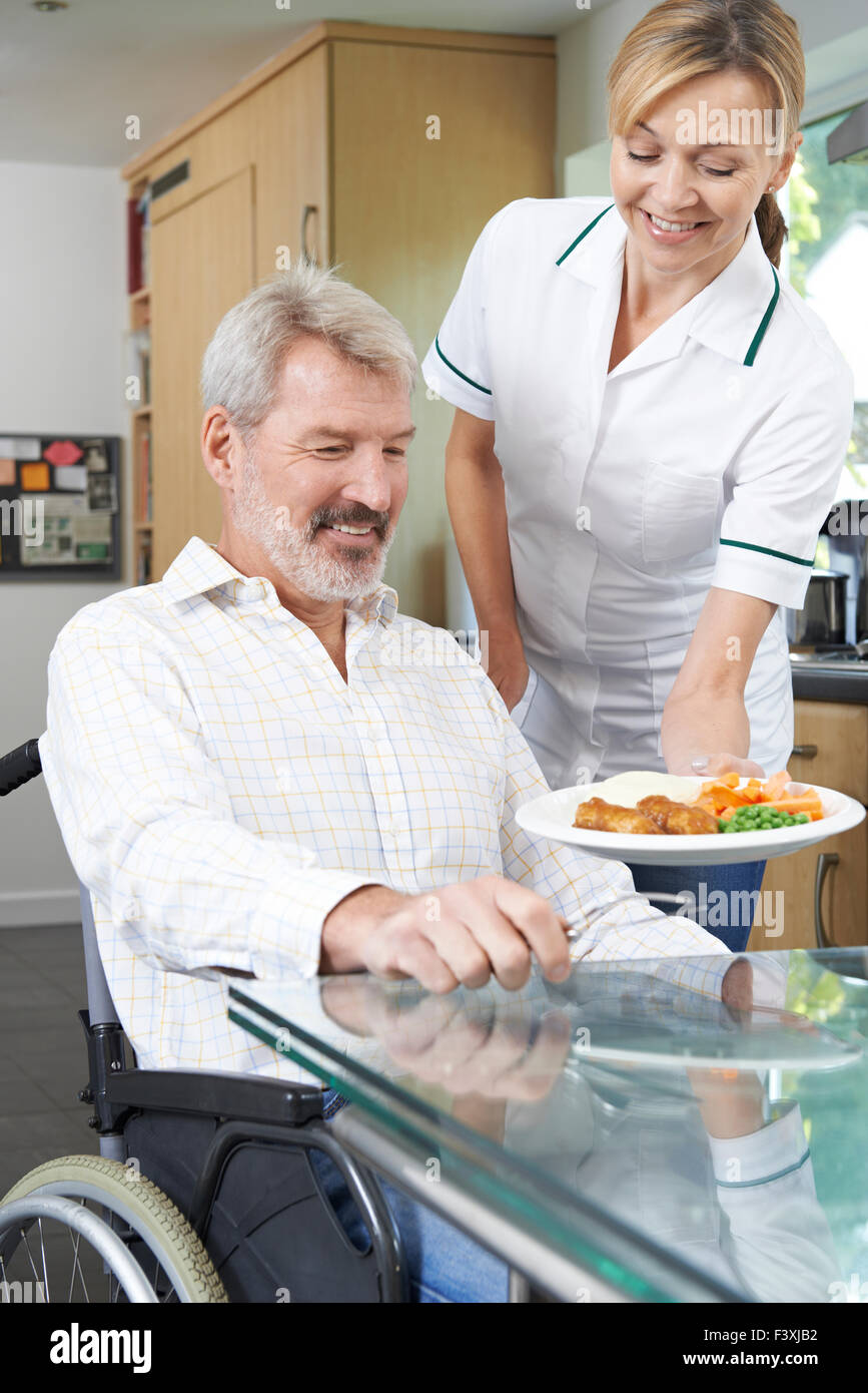 Pflegeperson servieren Mahlzeit Mann im Rollstuhl zu Hause Stockfoto