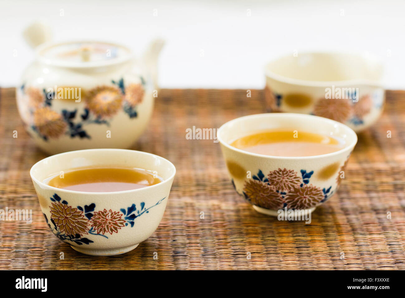 Japanischen chrysantheme eingerichtet Kaffee Service, eingestellt. Teekanne, zwei handless Tassen mit Tee gefüllt, und Schüssel mit grünem Tee auf Reed mat. Stockfoto
