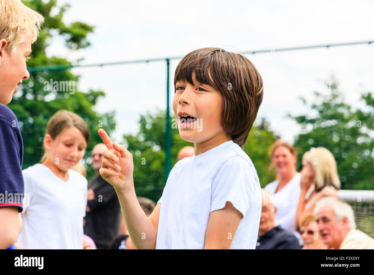 Kinder in der Schule Sport Tag, zwei Jungen im Alter von 10-11, aufgeregt und glücklich, ein Hinweis darauf, während im Gespräch mit den anderen. Beide trugen Sports top. Stockfoto