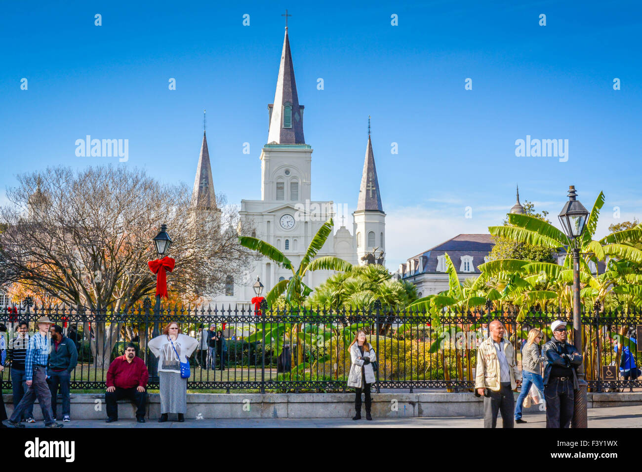 Schwarzer gusseiserner Zaun mit Menschen und roten Feiertagsbögen vor entfernten Türmen der St. Louis Cathedral am Jackson Square, New Orleans, LA Stockfoto