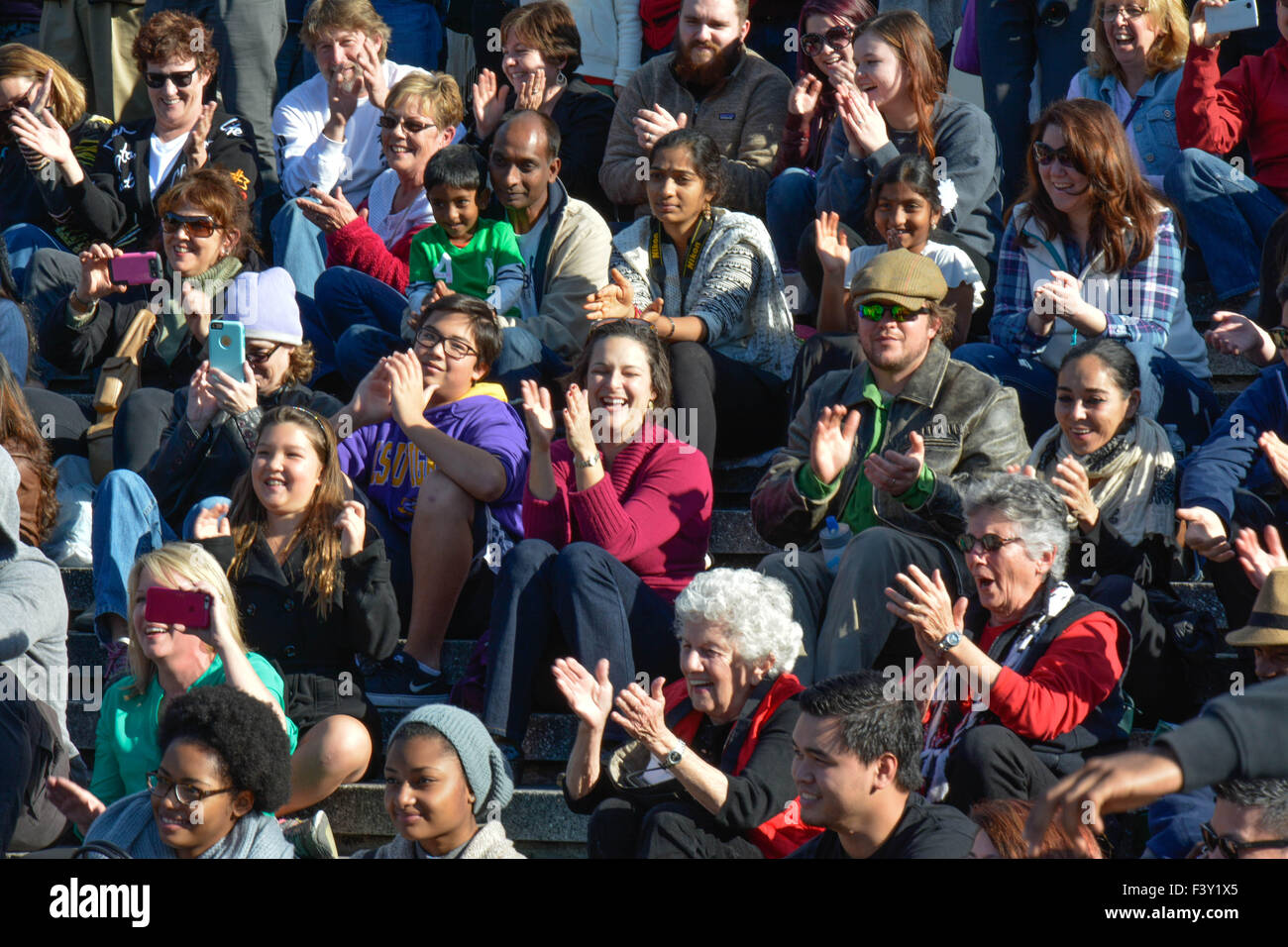 Eine Menge von ethnisch gemischten Menschen in den USA sitzen zusammen auf der Tribüne, lachen, applaudieren & beim Ansehen eines Ereignisses zu reagieren Stockfoto