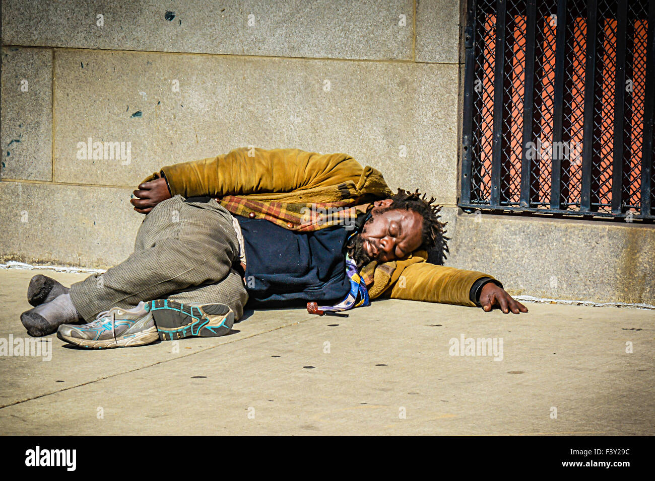 Ein schmutziger und Obdachloser Afroamerikaner Mann schläft leider auf einem Bürgersteig auf einer Stadtstraße in den USA Stockfoto