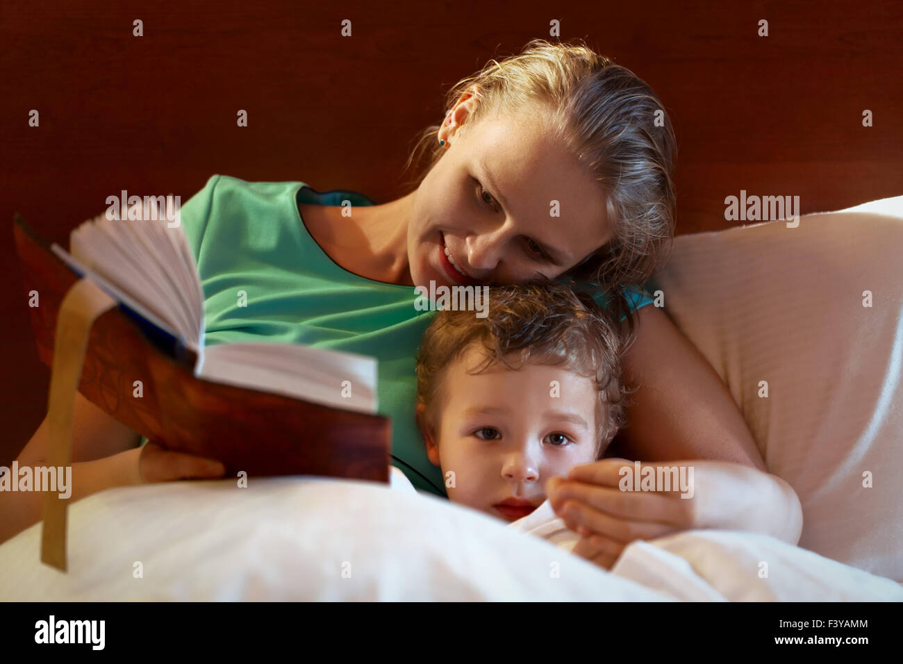 Junge Mutter ihr Kind im Bett lesen Stockfoto