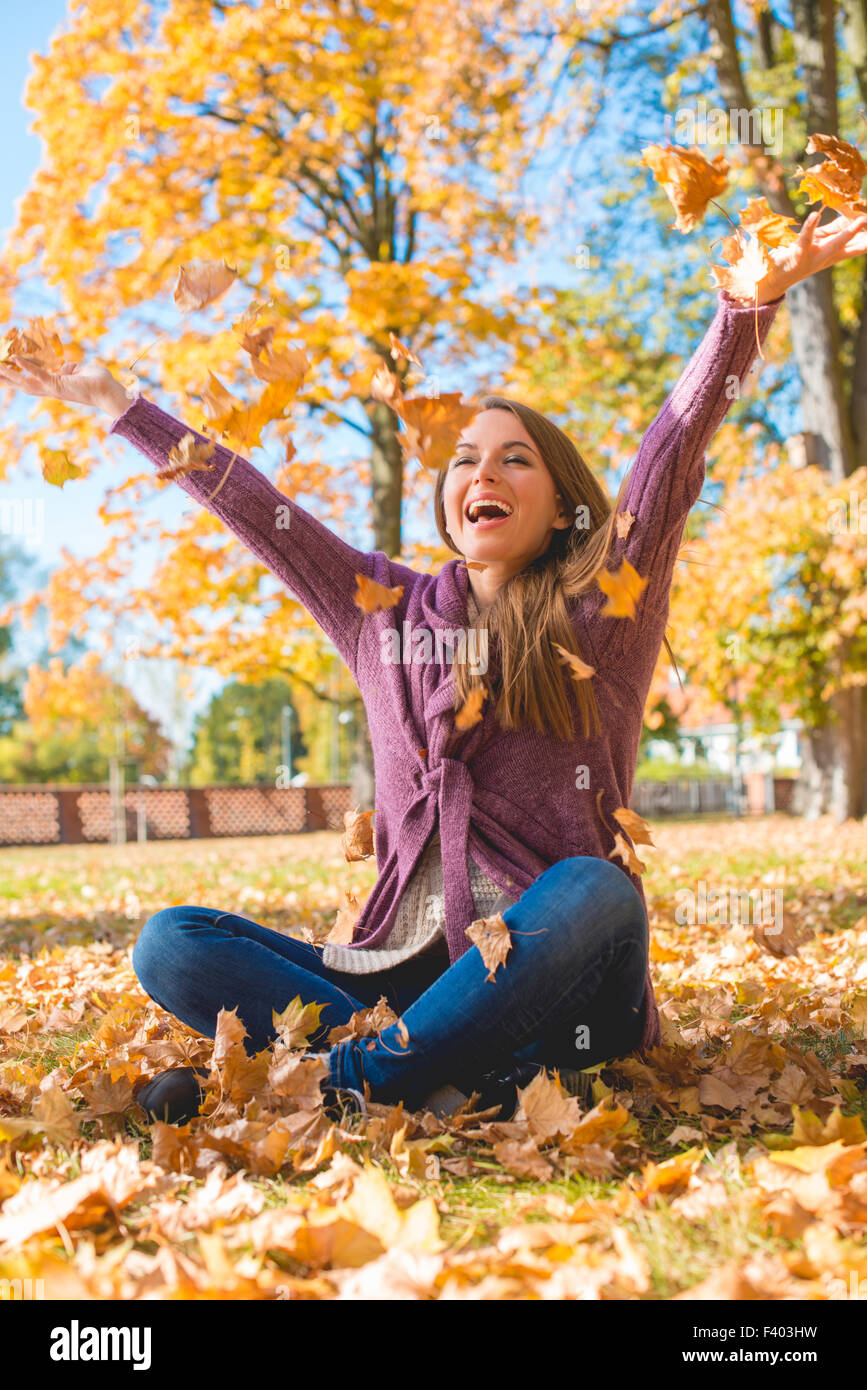 Glückliche Frau sitzt am Boden spielen trockene Blätter Stockfoto