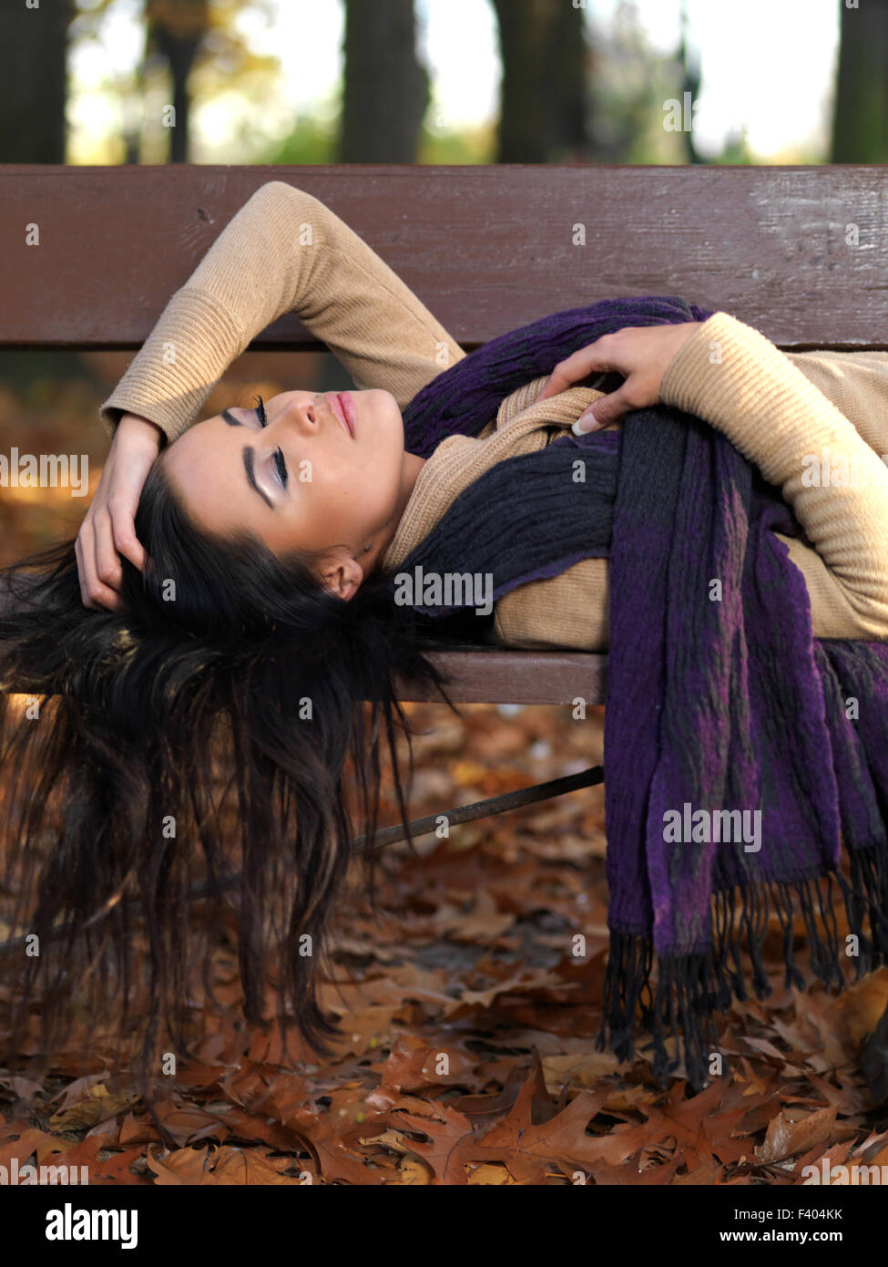 Lange Haare Frau schläft auf Bank im Herbst-Outfit Stockfoto