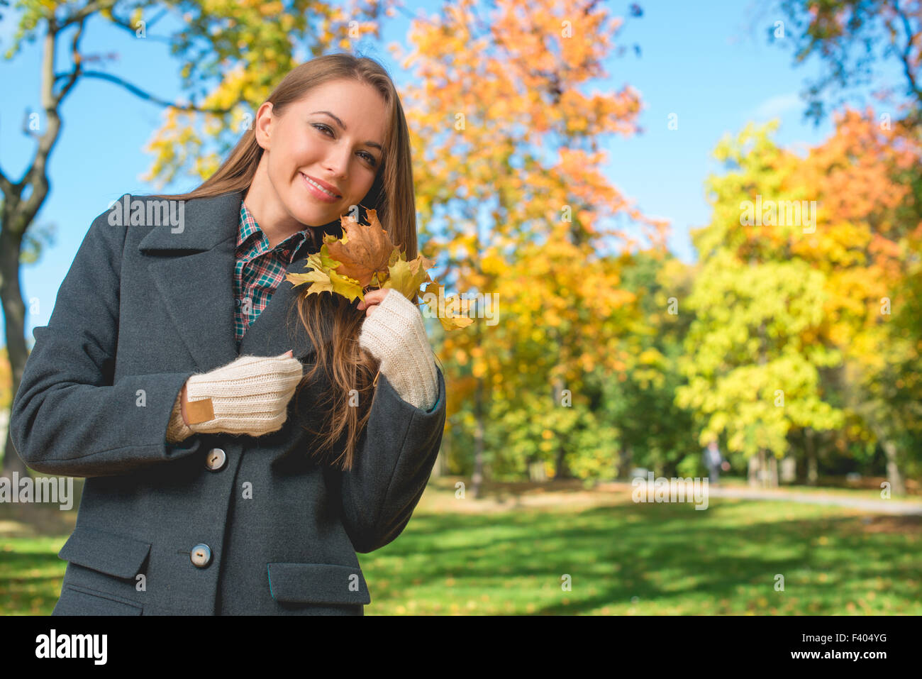 Blonde Frau im grauen Mantel hält trockene Blätter Stockfoto