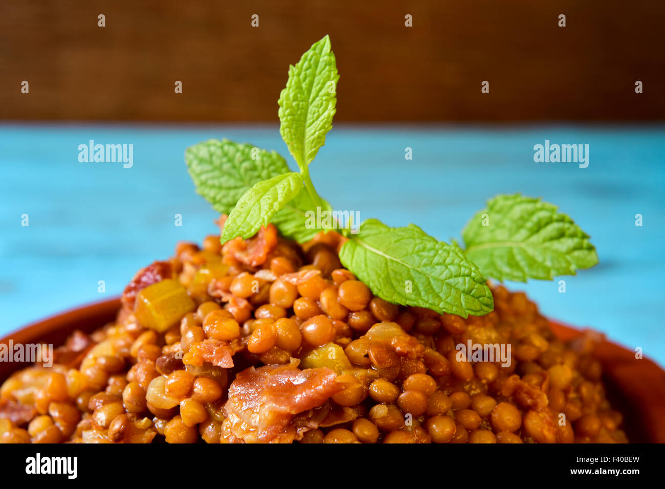 Nahaufnahme einer Steingut-Schale mit spanischen Linsen-Eintopf mit Serrano-Schinken auf einem blauen rustikalen Holztisch Stockfoto