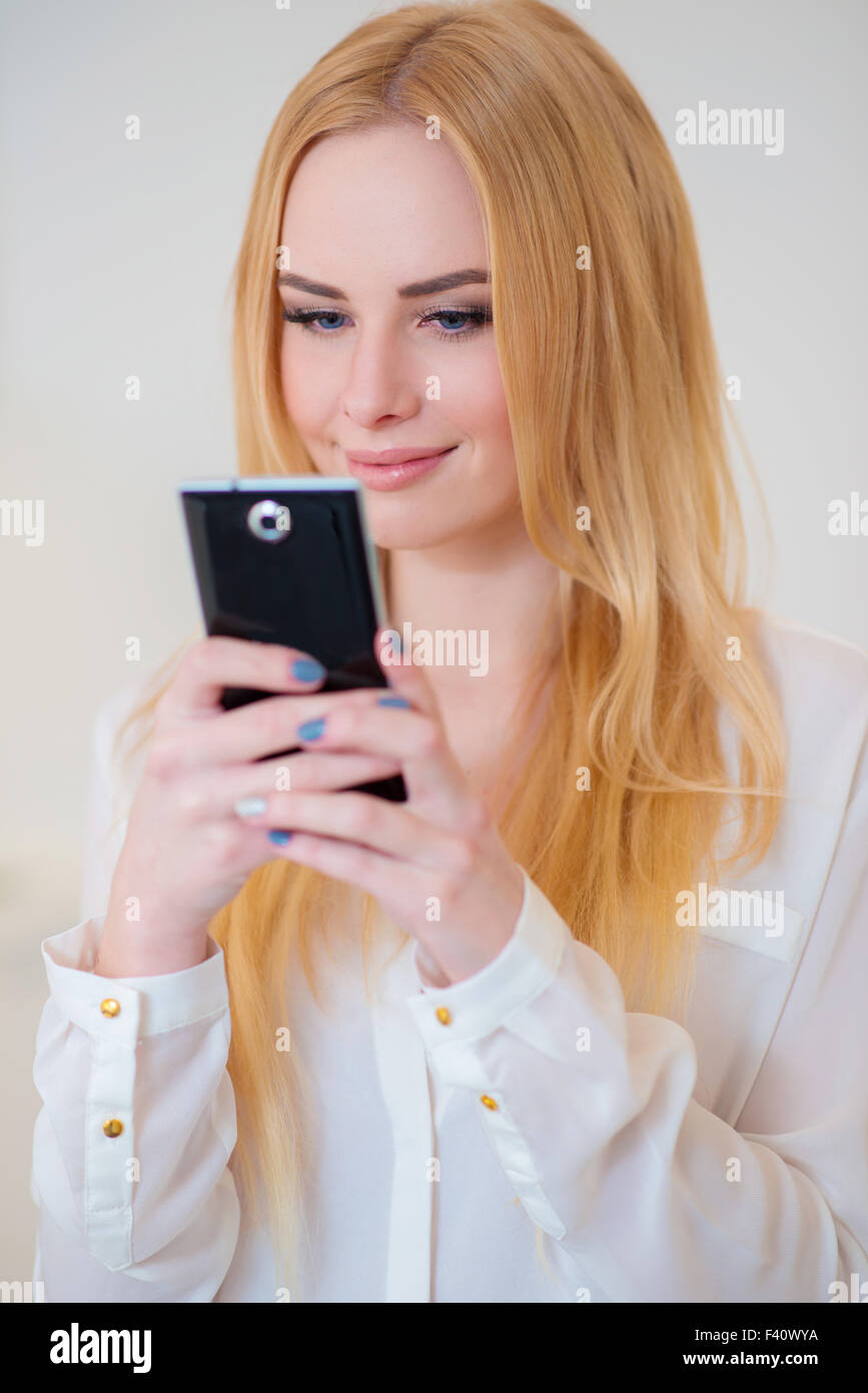 Lächelnde blonde Frau mit Hilfe ihres Mobiltelefons Stockfoto