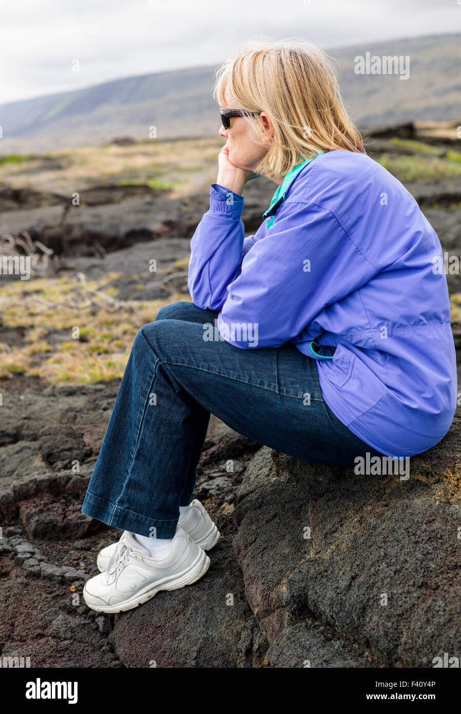 Weibliche Touristen sitzen auf Lavafelsen entlang der Küste, Hawaii Volcanoes National Park, Big Island, Hawaii, USA Stockfoto