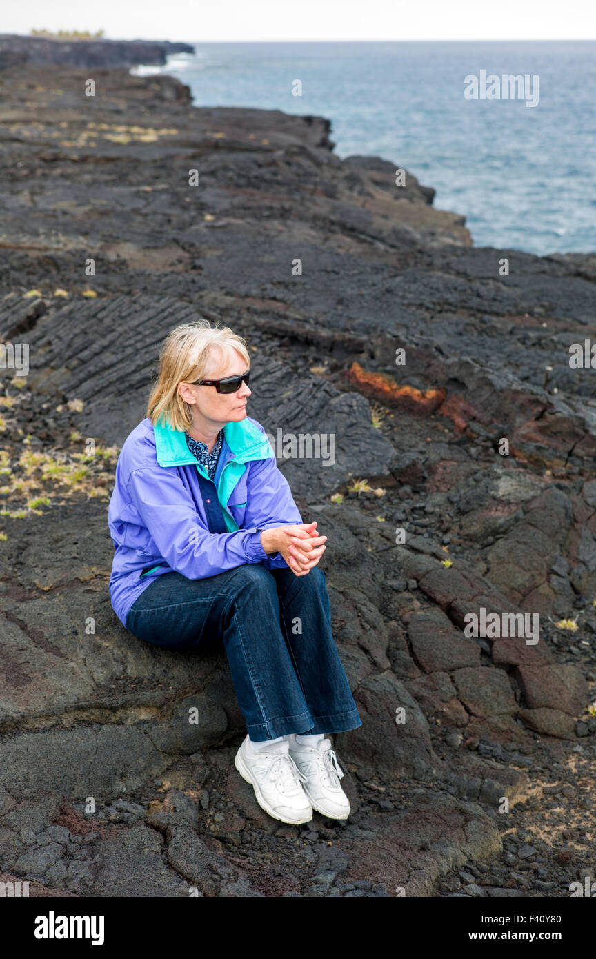 Weibliche Touristen sitzen auf Lavafelsen entlang der Küste, Hawaii Volcanoes National Park, Big Island, Hawaii, USA Stockfoto