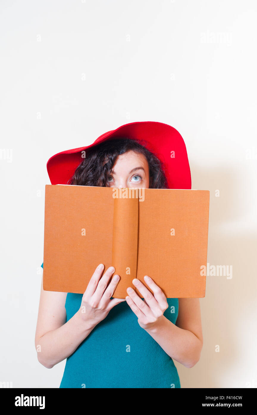 Junge Frau mit roten Hut und blauen Augen, die nach oben mit einem Buch auf ihrem Gesicht Stockfoto