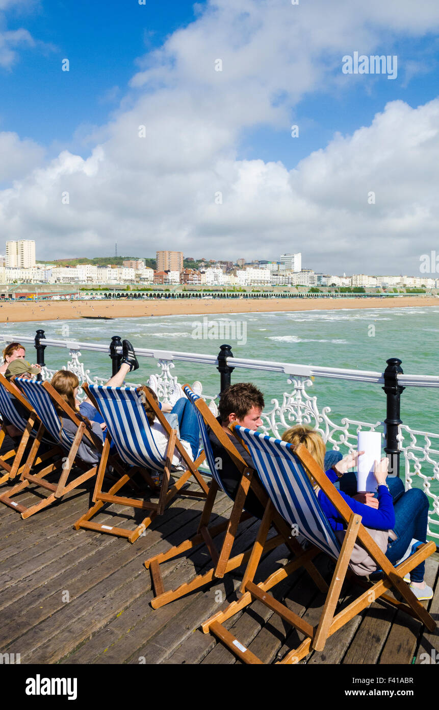 Leute sitzen in Liegestühlen auf Brighton Pier mit Blick auf das Meer und den Strand von Brighton. East Sussex, England. Stockfoto