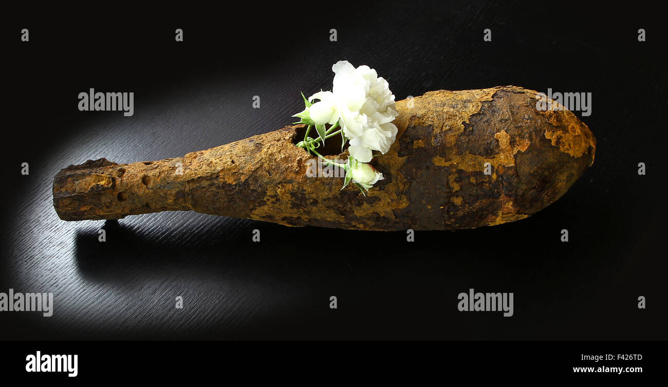 Vintage verrostet Luftfahrt Bombe erschossen Projektil Schale, die dem zweiten Weltkrieg mit Blumen im Loch auf schwarzen Tisch explodierte Stockfoto