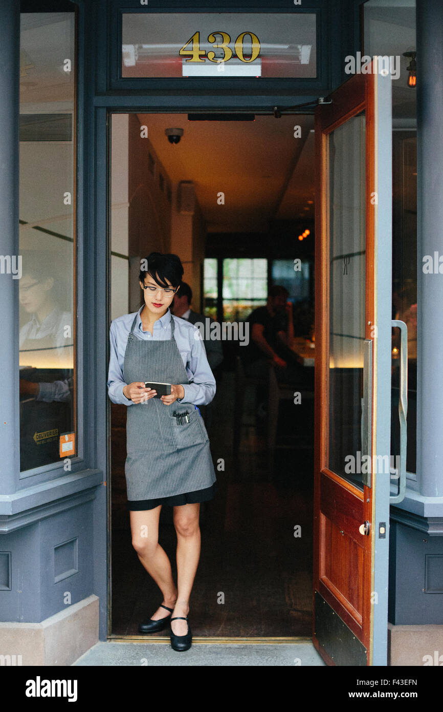 Junge Kellnerin trägt eine Schürze in einem Stadtrestaurant. Stockfoto