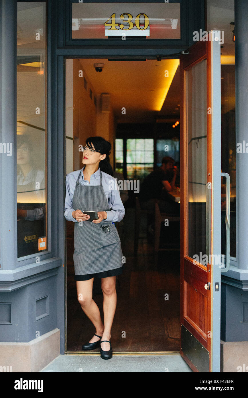 Junge Kellnerin trägt eine Schürze in einem Stadtrestaurant. Stockfoto
