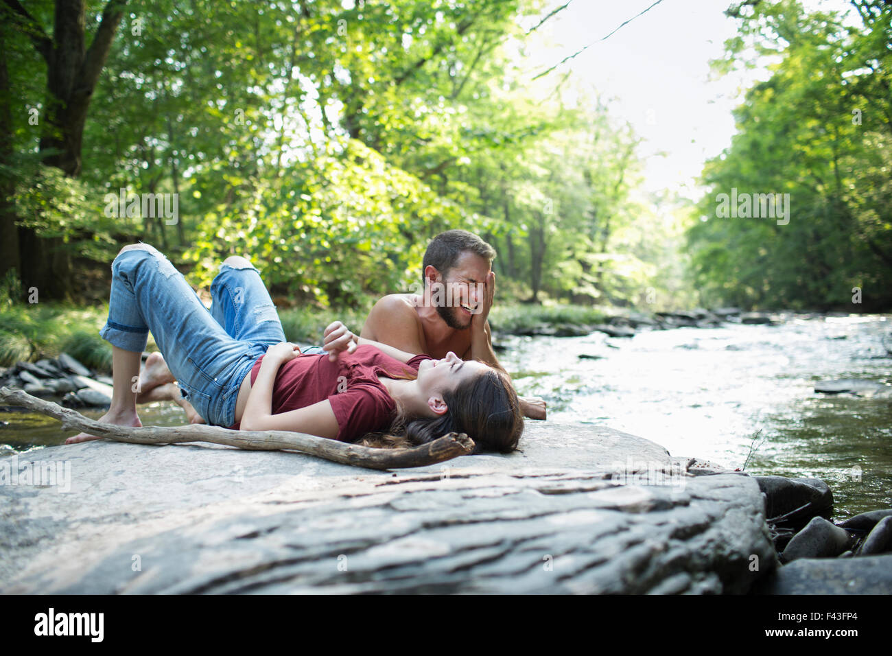Ein junger Mann und eine Frau liegend auf den Felsen am Ufer eines Flusses. Stockfoto