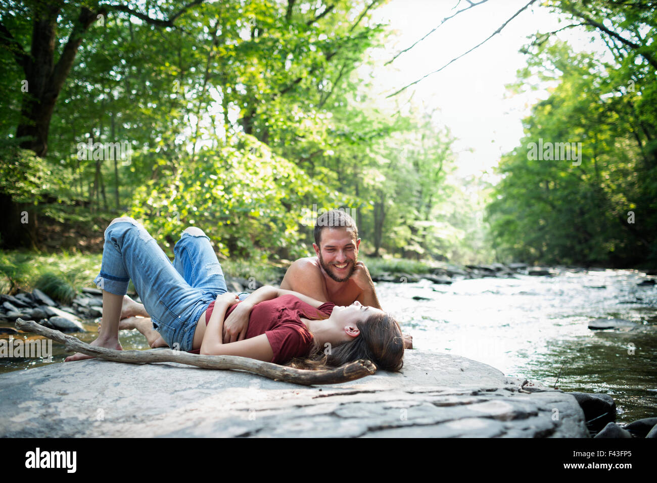 Ein junger Mann und eine Frau liegend auf den Felsen am Ufer eines Flusses. Stockfoto