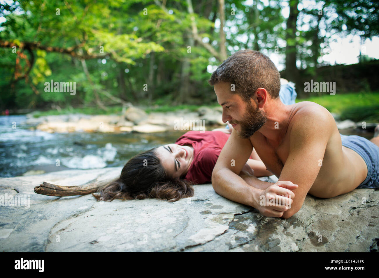 Ein junger Mann und eine Frau liegend auf den Felsen am Ufer eines Flusses. Stockfoto