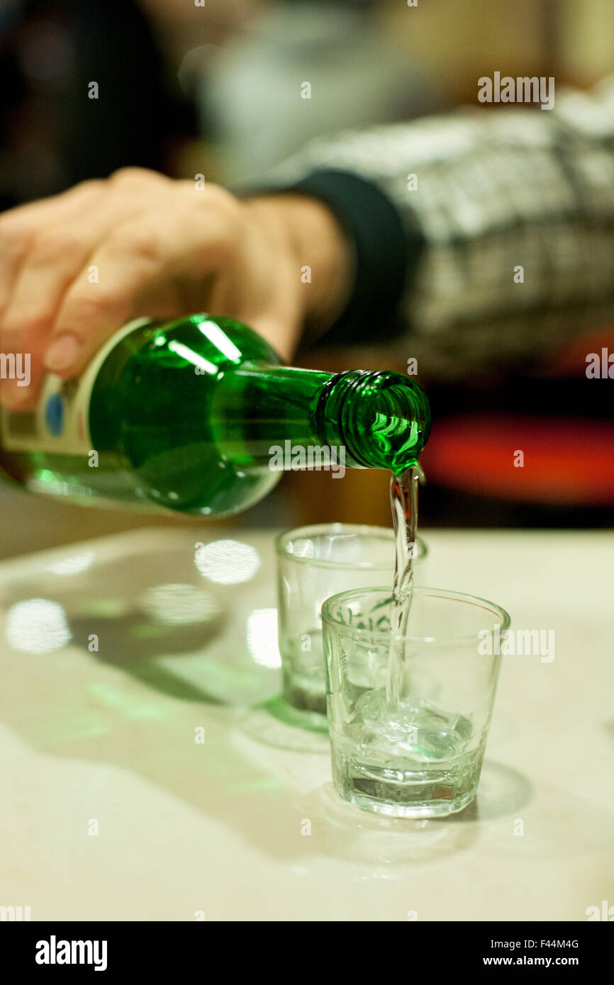 Grüne Flasche mit klarer Flüssigkeit ausgegossen in Shot-Glas Stockfoto