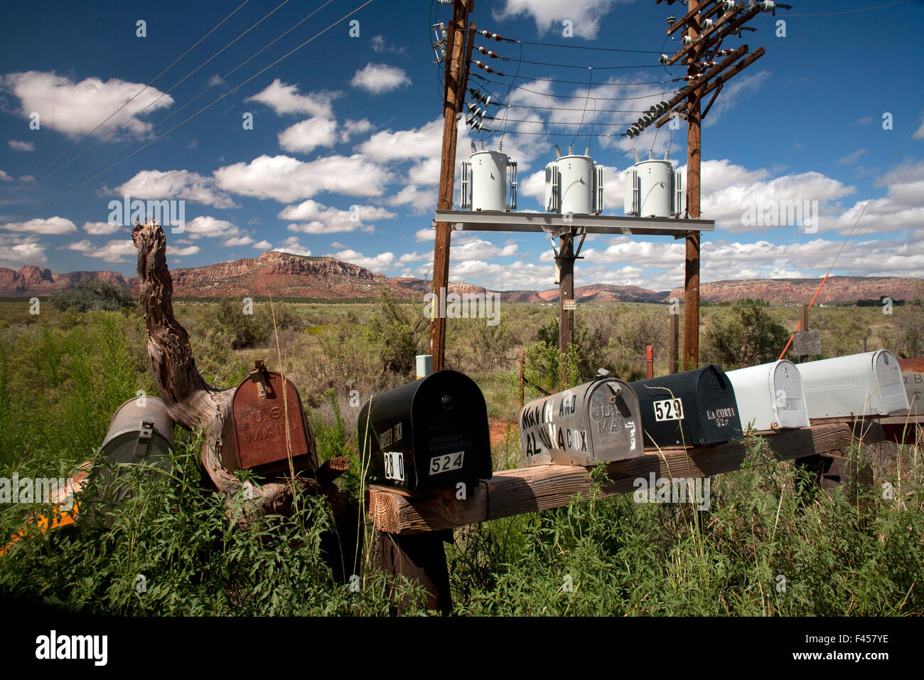Eine Reihe von nummerierten Postfächer ist mit elektrischen Transformatoren auf einem ländlichen Lane in Cane Betten, AZ. Hinweis Butte im Hintergrund gegenübergestellt. Stockfoto