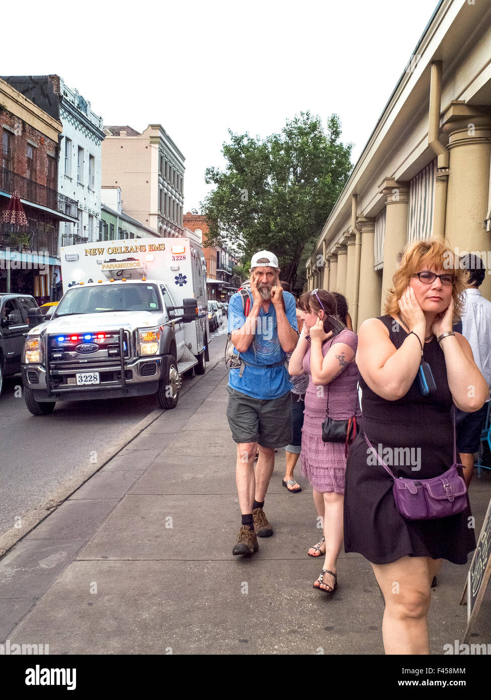 Fußgänger außerhalb des berühmten französischen Marktes in New Orleans, LA, die ihre Ohren wie ein Krankenwagen mit eine laute Sirene ihnen auf der Straße geht. Stockfoto